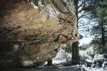 Shirtless man climbing on rock formation in forest - CAVF18201