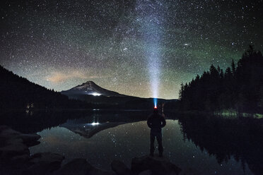 Silhouette man wearing headlamp standing at lakeshore against starry sky - CAVF18206