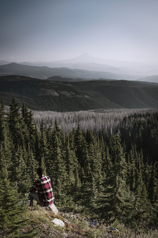 Wanderer sitzt bei Bäumen und Bergen gegen den Himmel, lizenzfreies Stockfoto