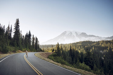 Junge fährt Skateboard auf der Straße zwischen Bäumen und Himmel im Mt. Rainier National Park - CAVF18223