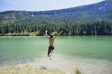 Rückansicht eines Mannes, der gegen einen Berg in einen See springt - CAVF18226