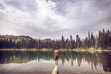 Rückansicht eines Jungen, der auf einem Holz am See steht, gegen einen bewölkten Himmel - CAVF18227