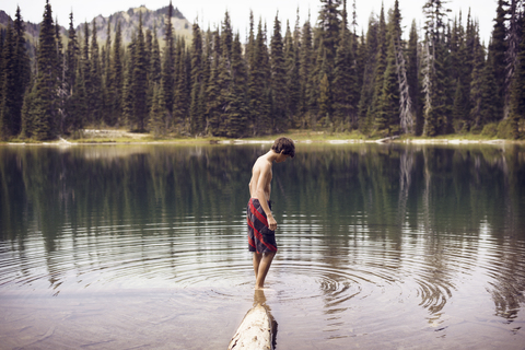 Seitenansicht eines am See stehenden Jungen vor Bäumen, lizenzfreies Stockfoto