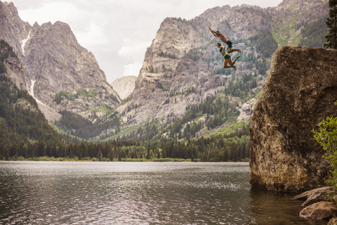 Freunde springen von einer Klippe im Grand Teton National Park in den See, lizenzfreies Stockfoto