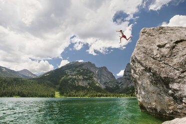 Low angle view of teenager cliff jumping in lake against cloudy sky - CAVF18289