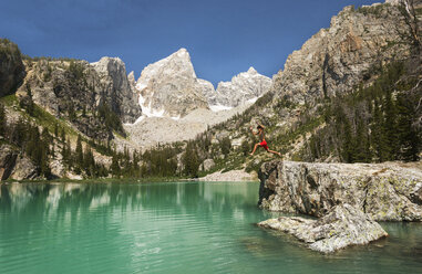 Teenage boy jumping into lake against mountains at dusk - CAVF18294