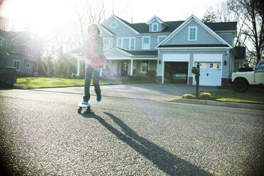 Junge fährt Skateboard auf der Straße mit Haus im Hintergrund - CAVF18313