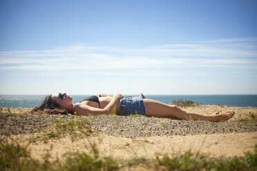 Seitenansicht einer Frau, die am Strand im Sand liegt, gegen den Himmel - CAVF18319