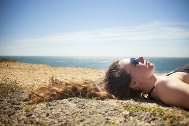 Headshot of woman lying on sand against sky - CAVF18320