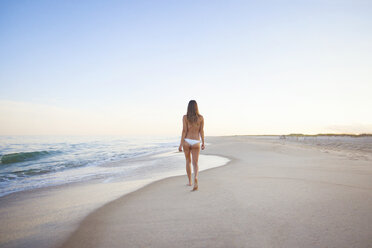 Rear view of woman walking on beach against clear sky - CAVF18334