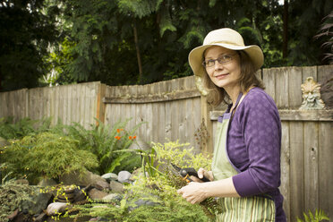 Porträt einer Frau, die eine Gartenschere hält, während sie im Garten steht - CAVF18351