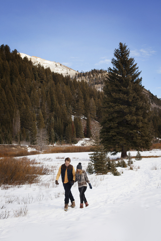 Junges Paar geht auf schneebedecktem Land gegen den Himmel, lizenzfreies Stockfoto