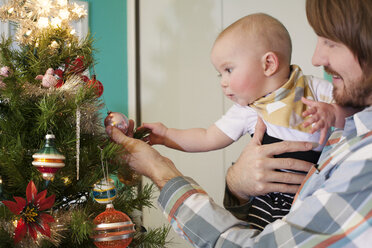 Vater zeigt Baby Schmuck am Weihnachtsbaum zu Hause - CAVF18501