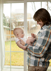 Side view of father playing with baby by window at home - CAVF18508