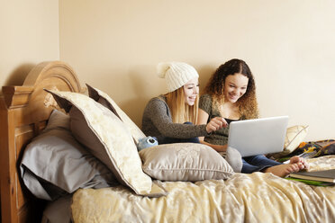 Glückliche Freunde, die einen Laptop benutzen, während sie zu Hause auf dem Bett sitzen - CAVF18511