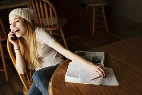 Fröhliches Teenager-Mädchen, das beim Lernen zu Hause ans Smartphone geht - CAVF18515