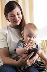 Mother and son using smart phone while sitting on sofa at home - CAVF18523