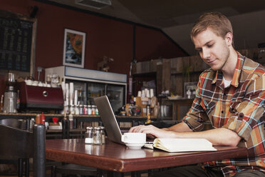 Mann arbeitet am Laptop, während er in einem Café sitzt - CAVF18530