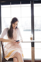 Frau, die ein Mobiltelefon benutzt, während sie in einem Café sitzt - CAVF18537