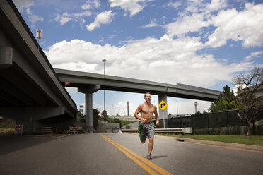 Männlicher Athlet läuft auf der Straße gegen den bewölkten Himmel - CAVF18572