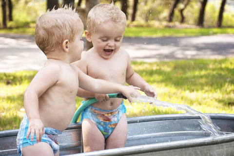 Fröhliche Zwillingsmädchen spielen mit Wasser in der Waschwanne, lizenzfreies Stockfoto