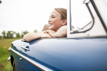 Happy girl sitting in car at field against sky - CAVF18686