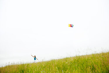 Girl holding kite and running on grassy field against clear sky - CAVF18690