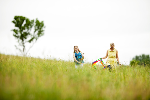 Glückliche Mutter und Tochter gehen auf einer Wiese gegen den klaren Himmel, lizenzfreies Stockfoto