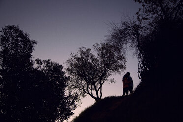 Low angle view of couple standing amidst silhouette trees against sky at dusk - CAVF18692