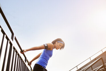 Seitenansicht einer Frau, die sich auf einem Geländer gegen den klaren Himmel streckt - CAVF18716
