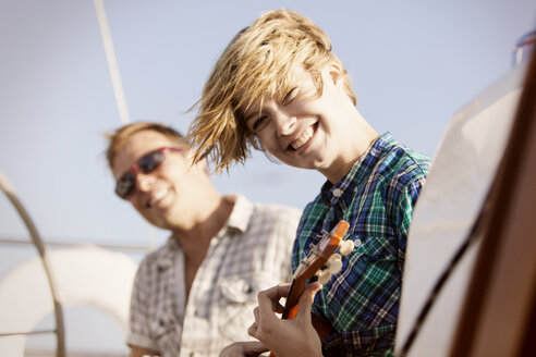 Glückliche Frau, die eine Gitarre hält, während sie mit einem Freund auf einem Boot reist - CAVF18775
