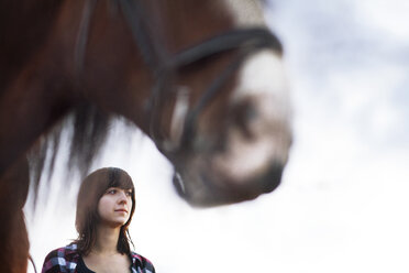 Niedriger Blickwinkel von Frau stehend durch Pferd gegen Himmel - CAVF18833