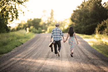 Rückansicht eines Paares, das sich an den Händen hält und an einem sonnigen Tag auf der Straße spazieren geht - CAVF18847