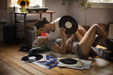 Romantischer Mann liegt mit einer Frau, die eine Schallplatte auf dem Boden hält, zu Hause - CAVF18876