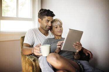 Junges Paar benutzt einen Tablet-Computer, während es zu Hause auf einem Sessel sitzt - CAVF18877
