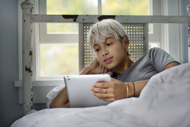 Young woman looking at tablet computer while relaxing on bed - CAVF18899