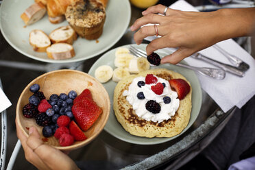 Cropped image of hands garnishing pancake with fruits and whipped cream on table - CAVF18912