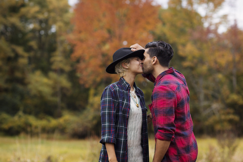 Zärtlicher Mann küsst Frau auf Feld im Herbst, lizenzfreies Stockfoto