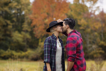 Affectionate man kissing woman on field during autumn - CAVF18919