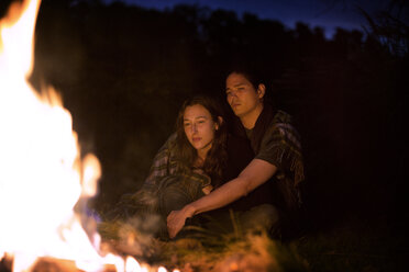 In eine Decke eingewickeltes Paar sitzt nachts am Lagerfeuer - CAVF18924