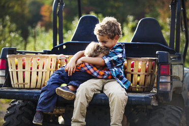 Brüder, die sich umarmen, während sie auf einem Geländewagen sitzen - CAVF18950