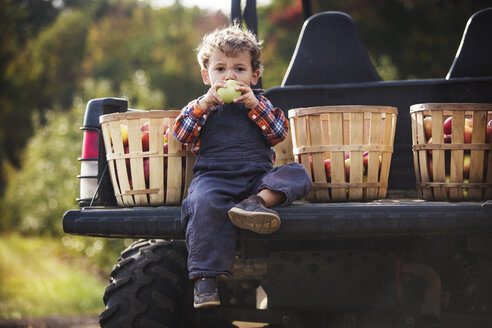 Porträt eines Jungen, der auf einem Geländewagen sitzend Obst isst - CAVF18951