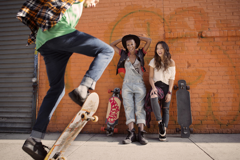 Freundinnen beobachten einen Mann bei einem Skateboard-Stunt, lizenzfreies Stockfoto