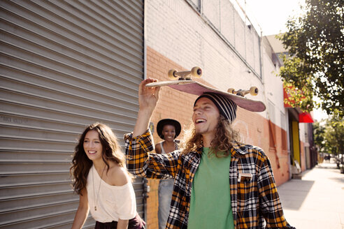 Mann trägt Skateboard auf dem Kopf beim Spaziergang mit Freundinnen - CAVF18996