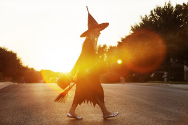 Girl dressed in witch costume walking on road during sunset - CAVF19062