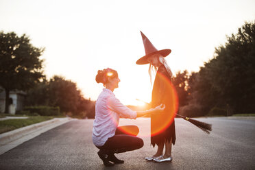 Woman dressing girl in witch costume during sunset - CAVF19063