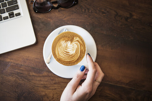 Ausgeschnittenes Bild von Hand mit Cappuccino auf Holztisch - CAVF19068