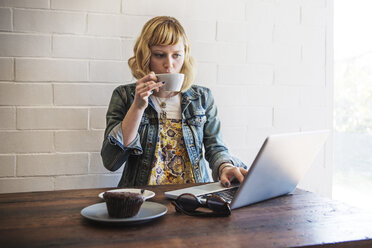 Frau trinkt Kaffee und benutzt einen Laptop in einem Café - CAVF19069