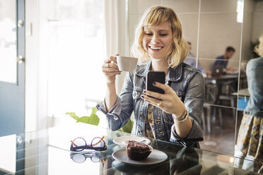 Happy woman using smart phone while standing in cafe - CAVF19070