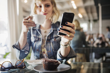 Frau hält Smartphone, während sie in einem Café steht - CAVF19071